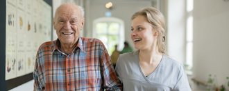 Schloss Hochaltingen Ein Bewohner und eine Mitarbeiterin gehen eingehakt über einen Flur.