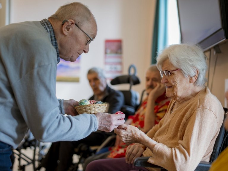Pfarrer Manfred F. (im Ruhestand) reicht einer Bewohnerin ein Osterei.