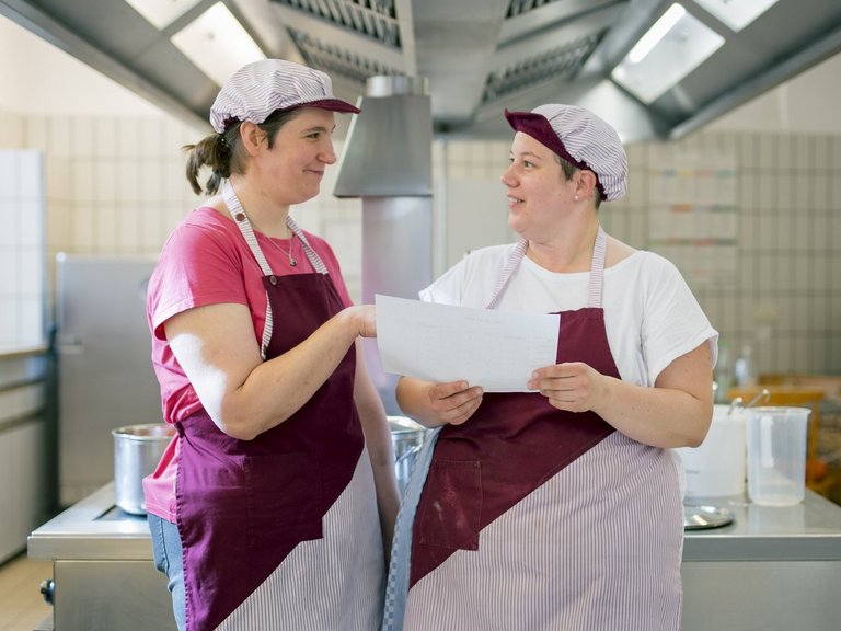 Zwei Mitarbeiterinnen tauschen sich angeregt in der Küche aus.