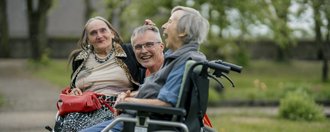 Schloss Hochaltingen Ein Mitarbeitender und zwei Bewohnerinnen sitzen im Garten und lachen in die Kamera.